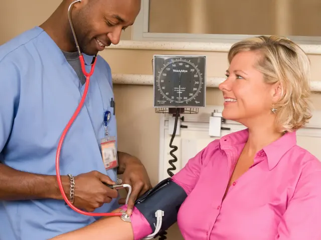 A nurse checking a smiling woman's blood pressure
